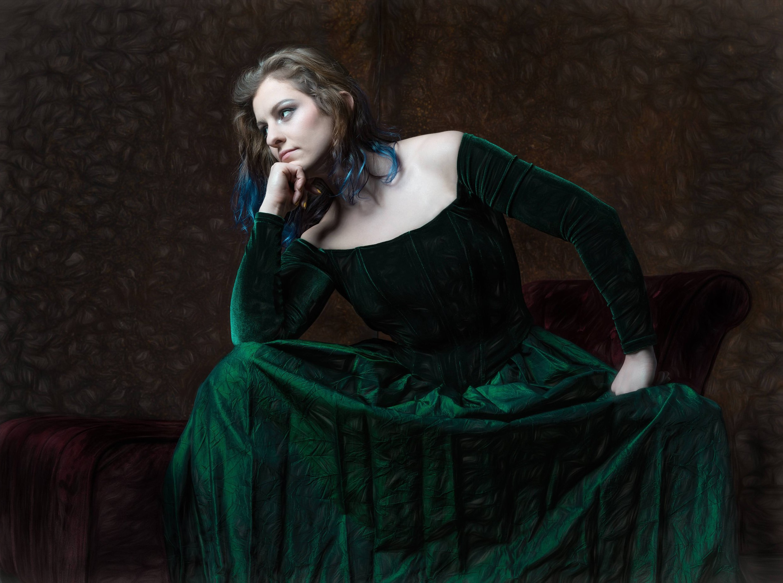 Portrait of Regan O'Brien in a green velvet gown, resting her chin on her hand, seated on a deep red chaise.